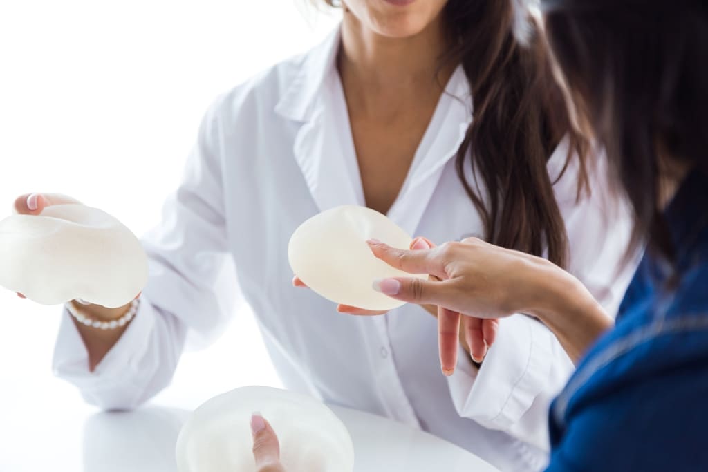 Doctor And Her Patient Choosing Mammary Prosthesis In The Office.